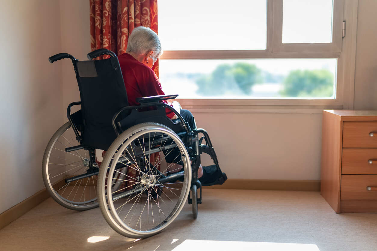 An elderly person in a wheelchair looking out a window in a nursing home, symbolizing potential nursing home abuse or neglect in Marietta.