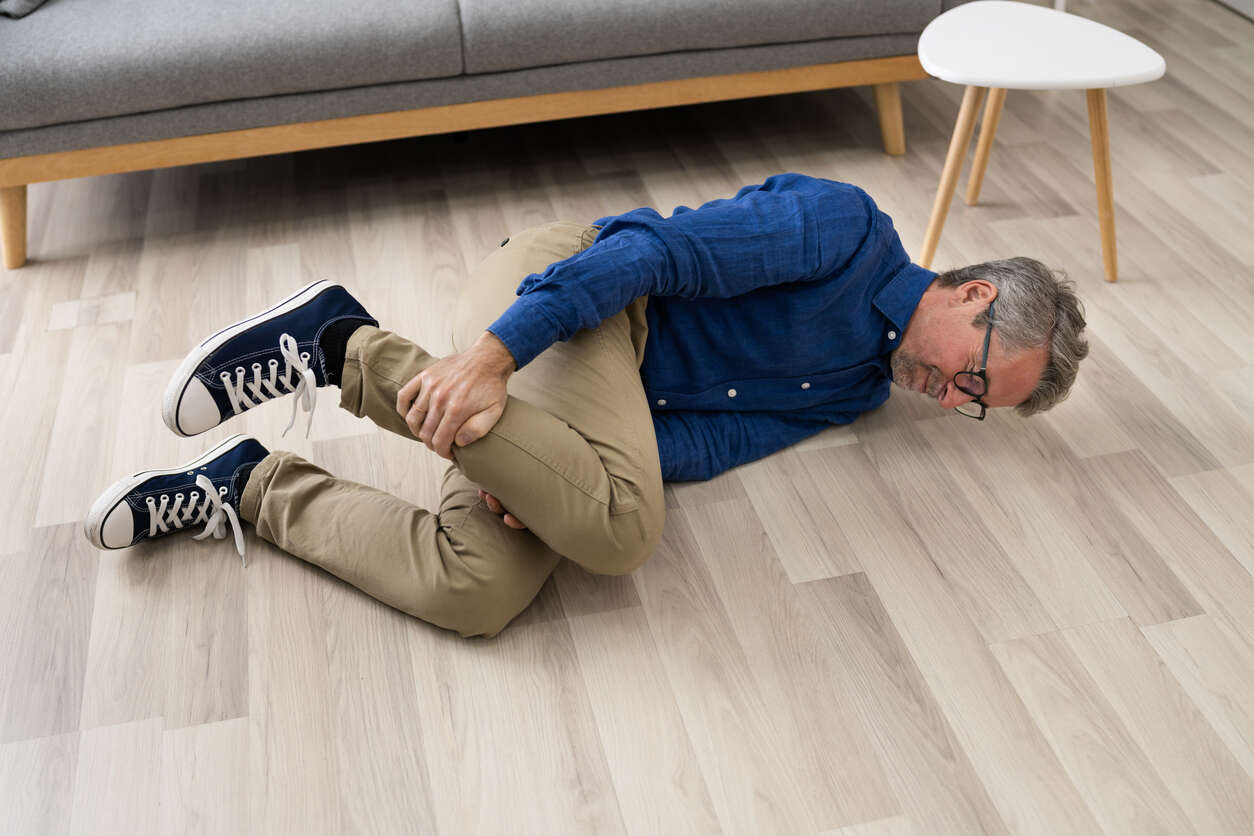 
A man lies on a light wood floor, clutching his leg in pain after a slip and fall. The image represents a Georgia premises liability case where an injury occurs on a property due to an unreasonably dangerous condition.