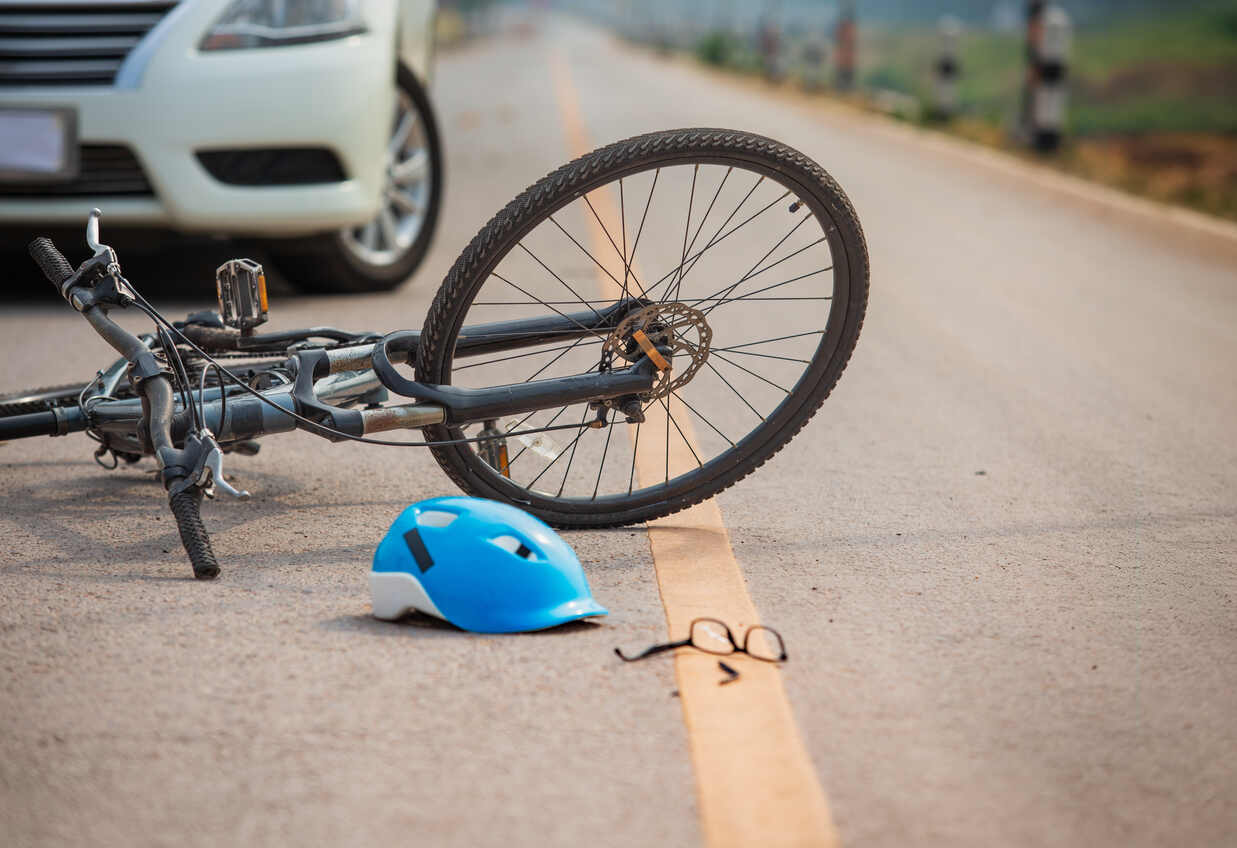 A bicycle lying on the road with a detached blue helmet and eyeglasses nearby, and a blurred white car in the background, signifying a bicycle accident.