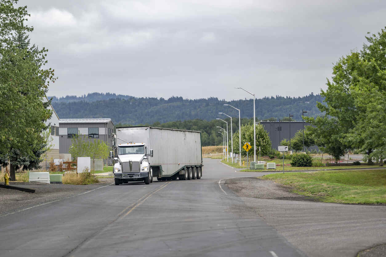 A large white semi-truck with a long silver trailer is making a wide turn on a two-lane road