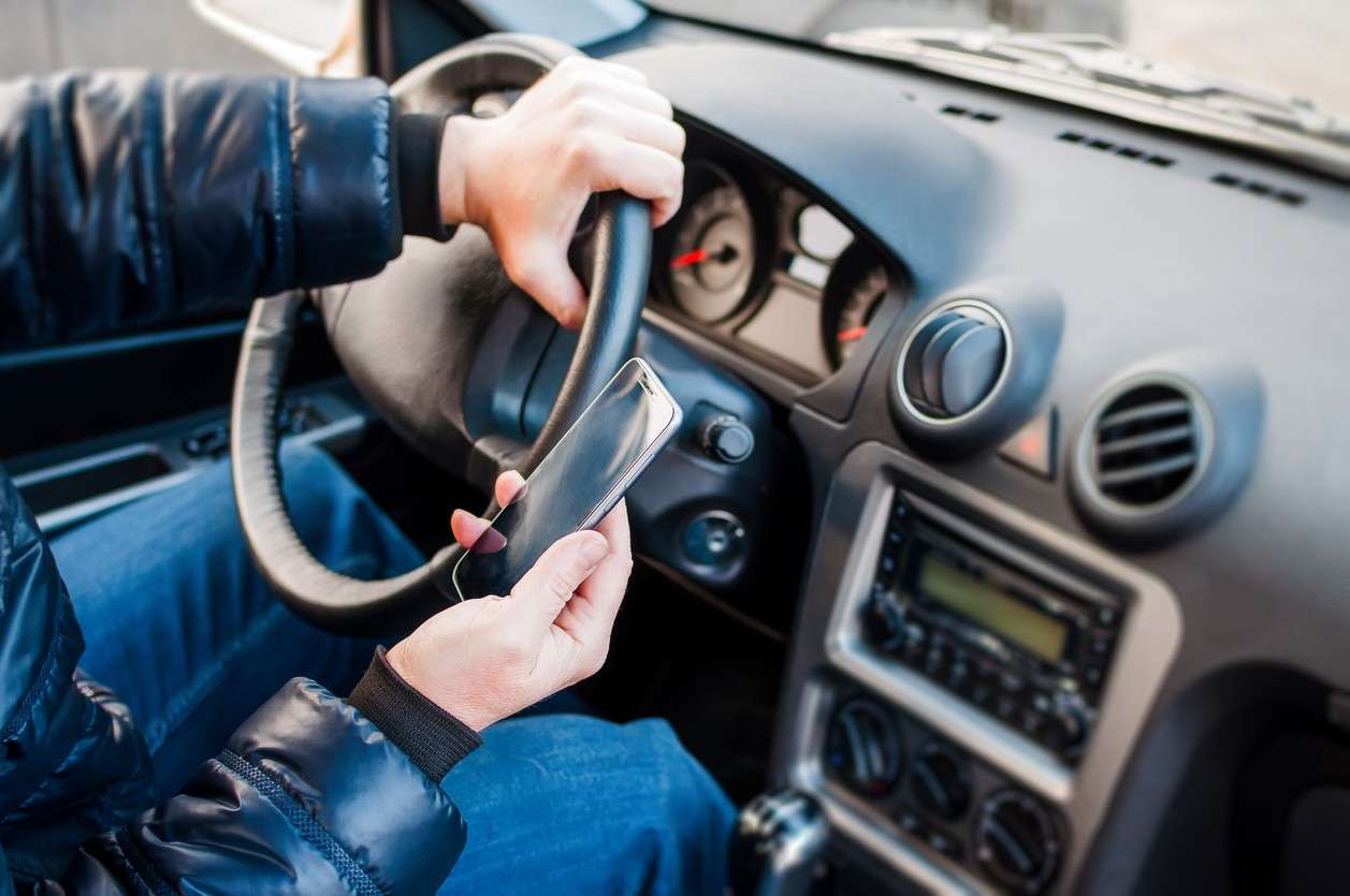 A person holding a smartphone while driving, symbolizing distracted driving and the evidence investigators seek beyond cell phone records.