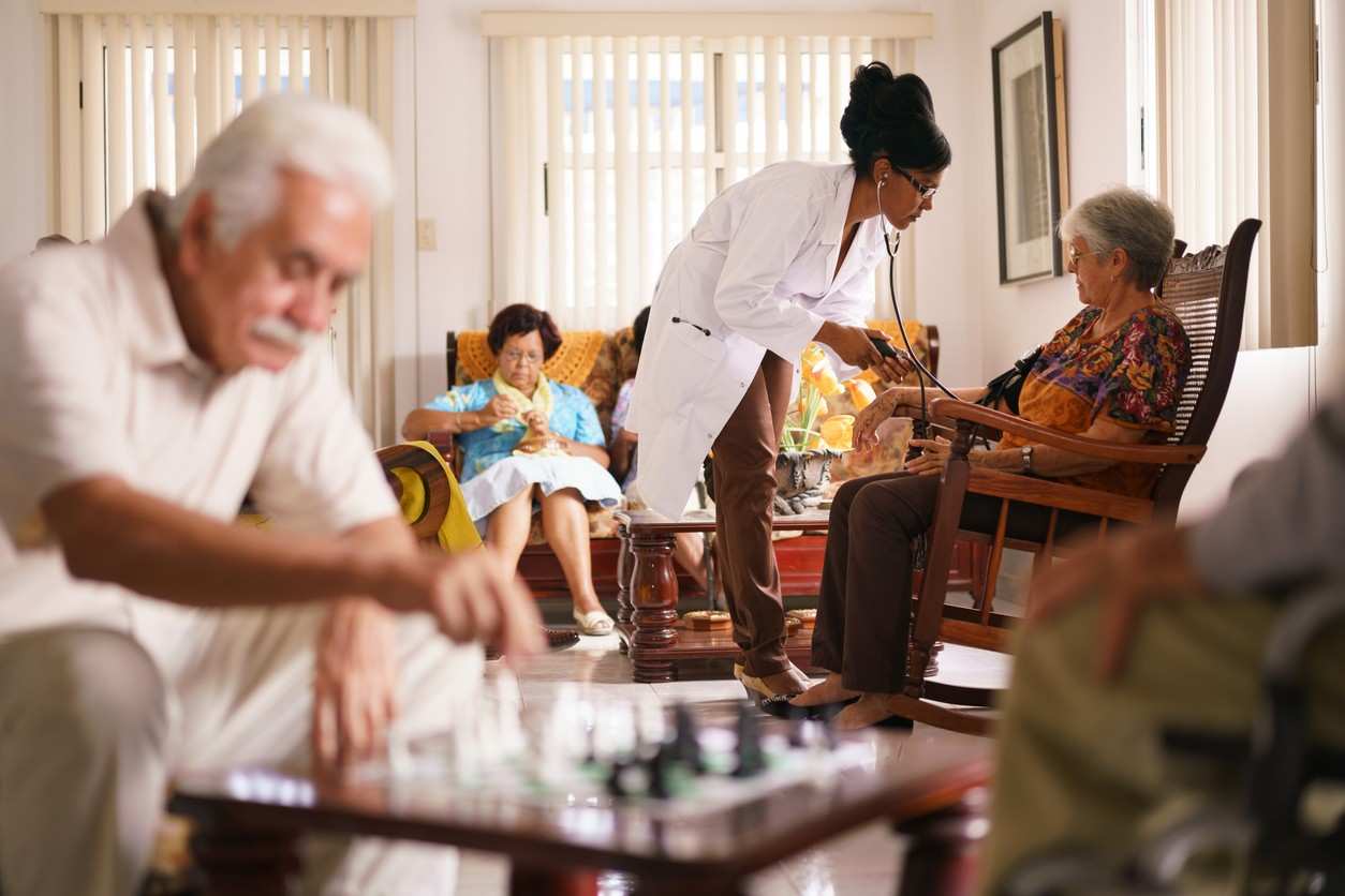 A healthcare worker attending to an elderly patient in a nursing home, symbolizing concerns of understaffing and resident harm.