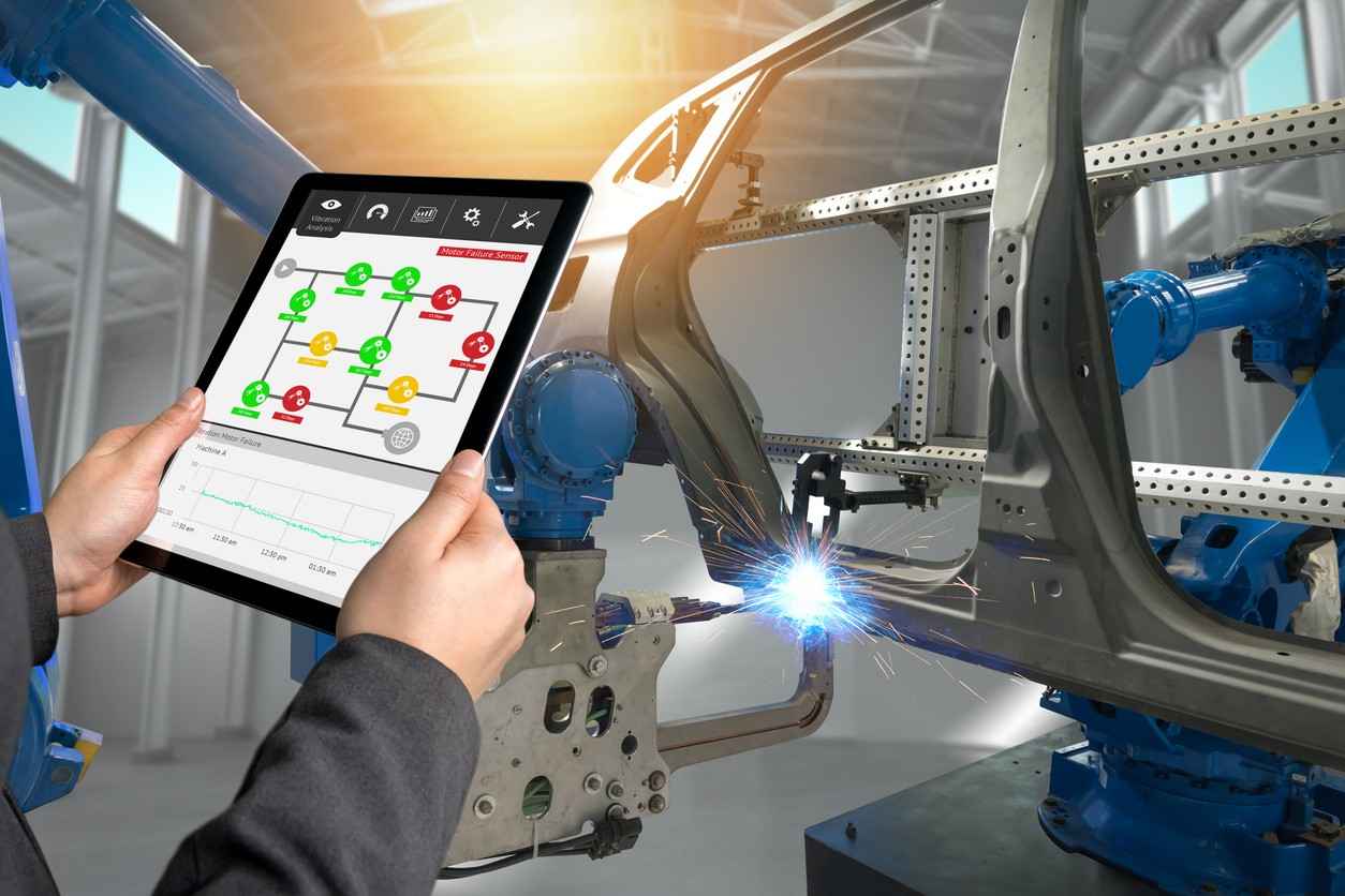 A person using a tablet to monitor industrial robots, symbolizing how software and sensor failures can contribute to preventable injuries.