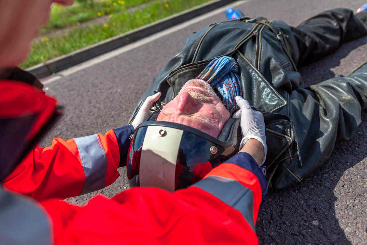 Emergency responders assisting an injured motorcyclist lying on the road, representing the challenges faced by motorcyclists in injury claims.