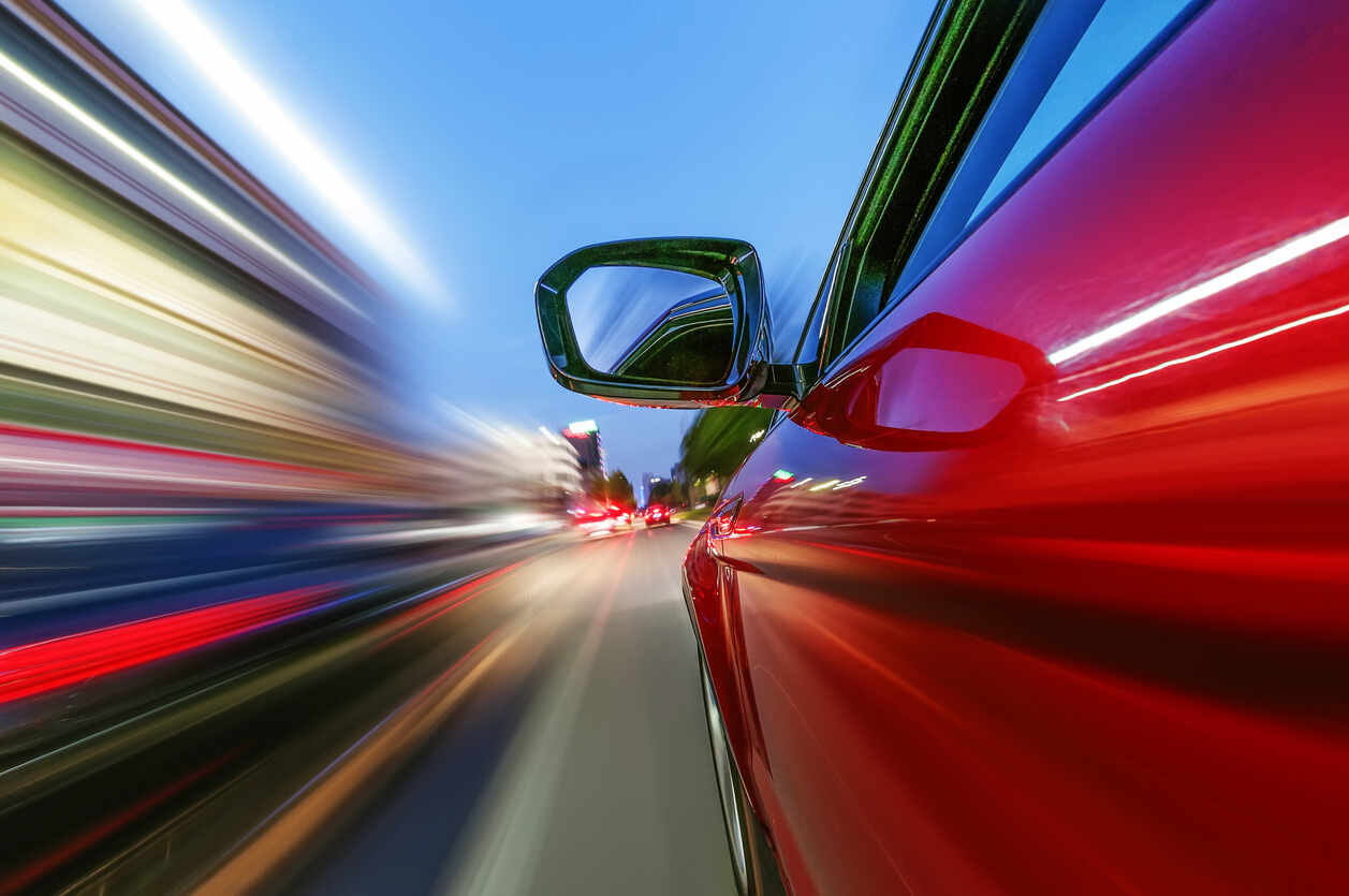 Close-up of a red car in motion on a city street at dusk, showcasing the concept of aggressive and reckless driving.
