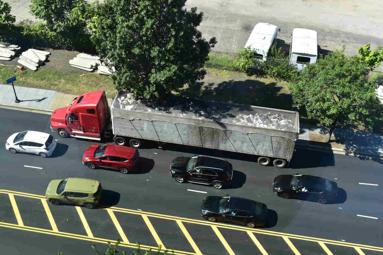 A red commercial truck with a large load driving on a busy road, with several cars in traffic, representing the potential risks of catastrophic rear-impact collisions involving commercial vehicles on I-285.