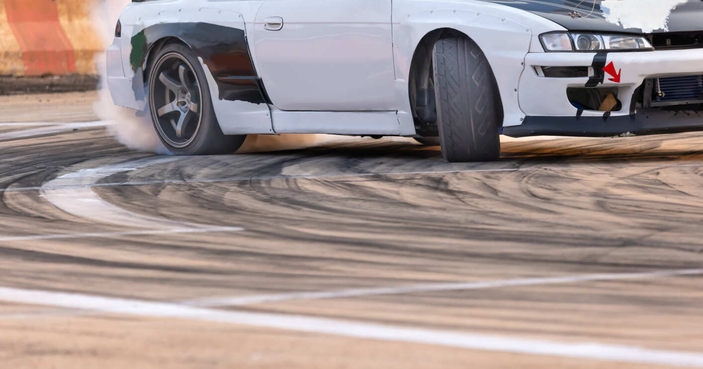 Car drifting across the center line on a racetrack, with smoke coming from the tires, symbolizing the dangers of drifting across lanes on Georgia's two-lane roads.