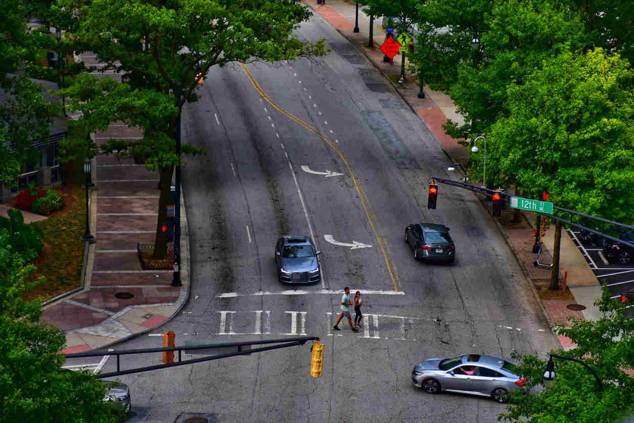Aerial view of an intersection in Georgia with cars making left turns and a pedestrian crossing, illustrating urban traffic with potential for illegal U-turns and left cross-turns.