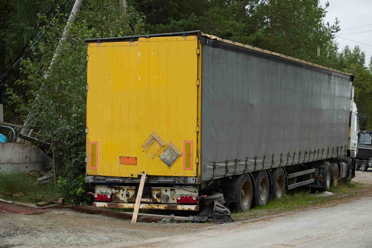 Damaged trailer parked on the side of the road, showing signs of wear and tear, representing the potential risks of trailer maintenance failures leading to highway accidents.